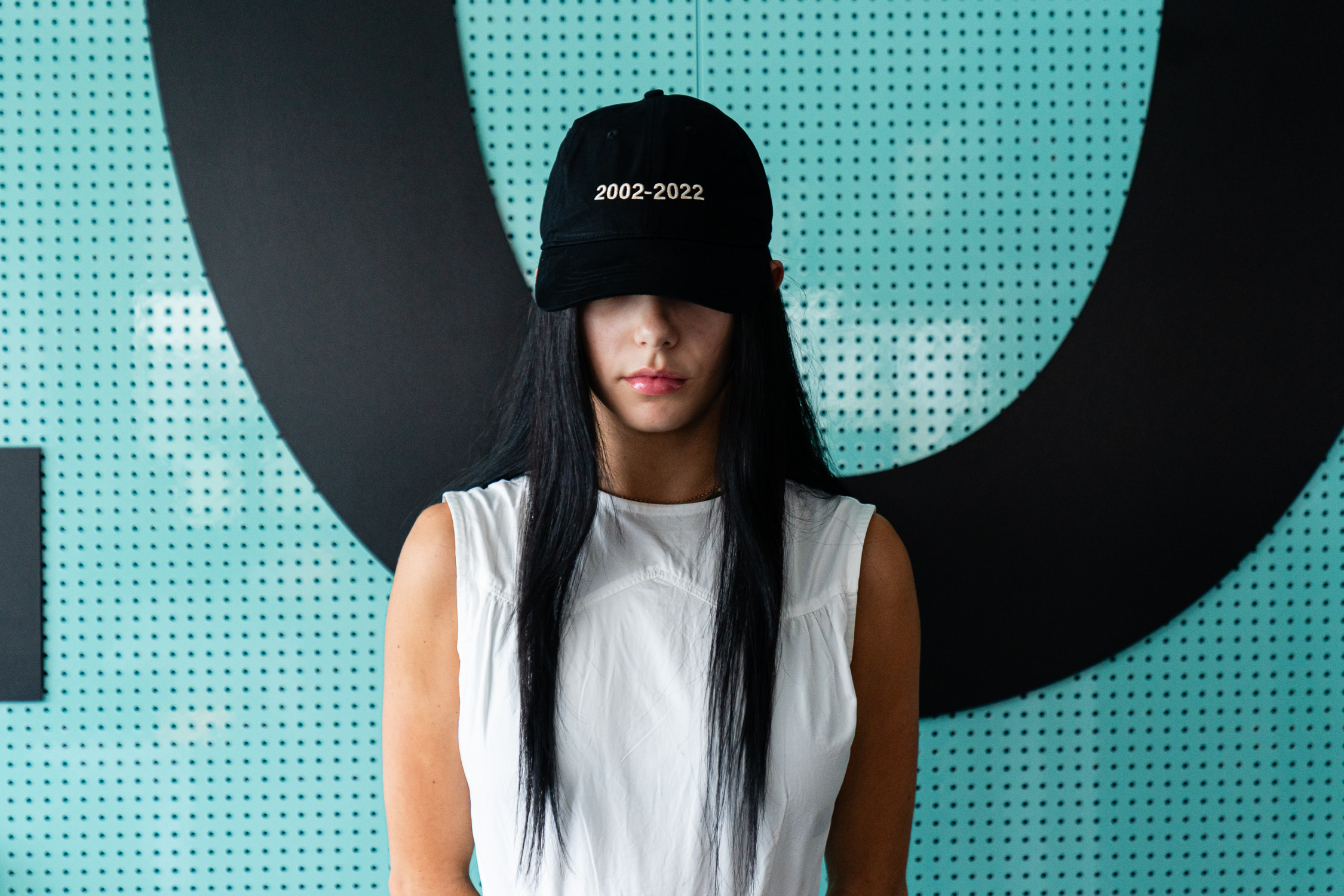 Model wearing a black Icebergs cap against a teal backdrop