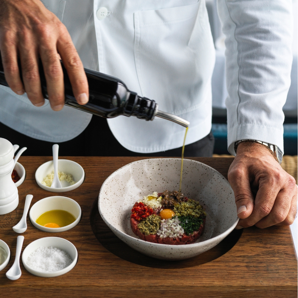 Chef finishing a tartare dish with olive oil at the pass