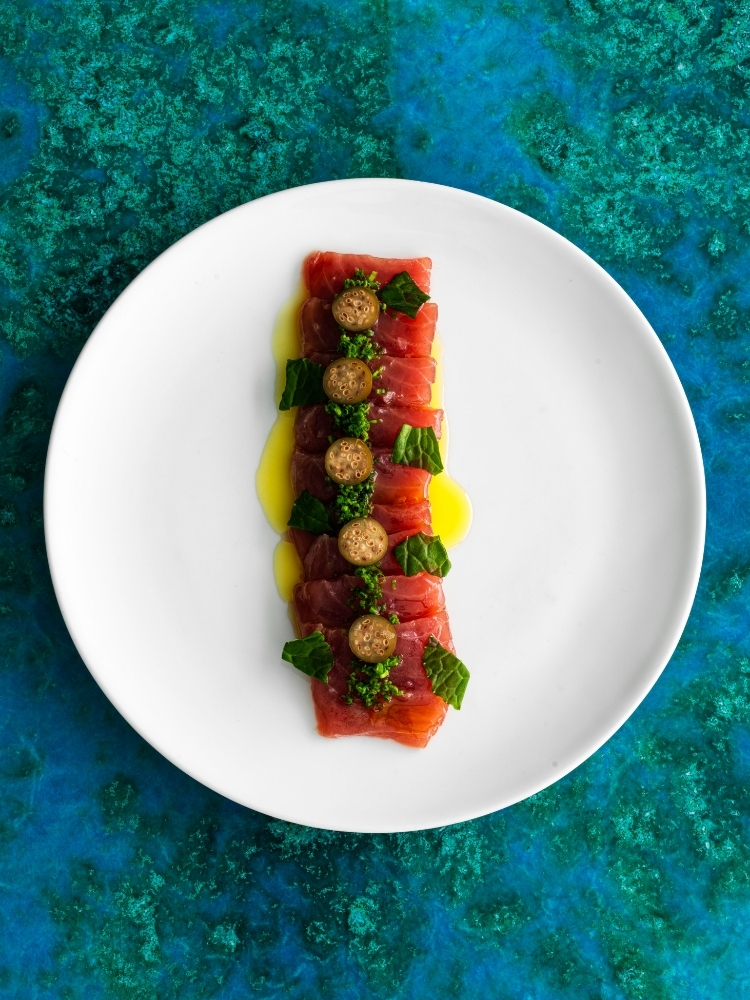 Cured fish plated in a line with garnishes on a white plate
