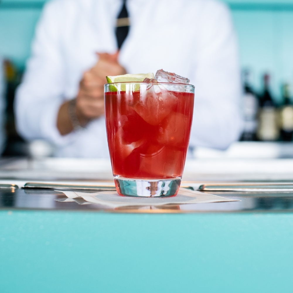 Red cocktail on the bar with a bartender behind