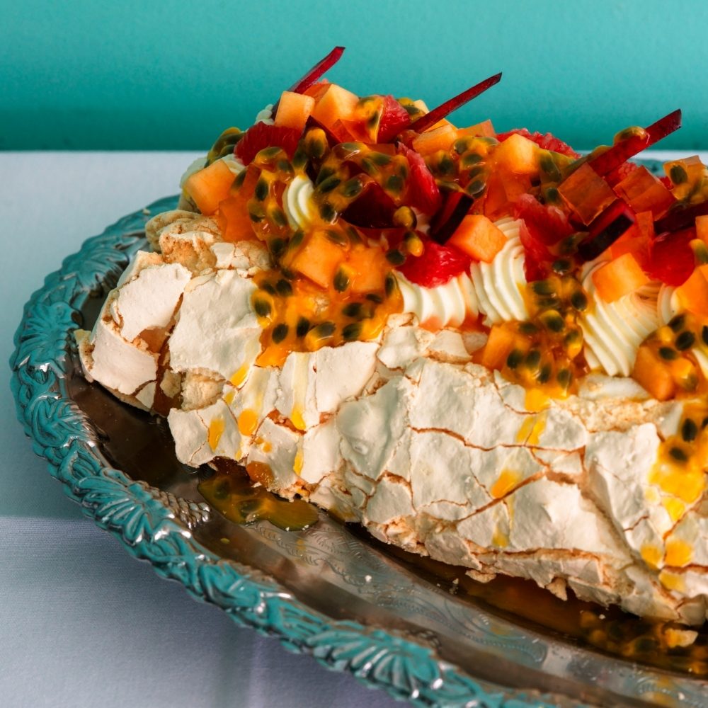 Pavlova topped with passionfruit and tropical fruit on a silver platter