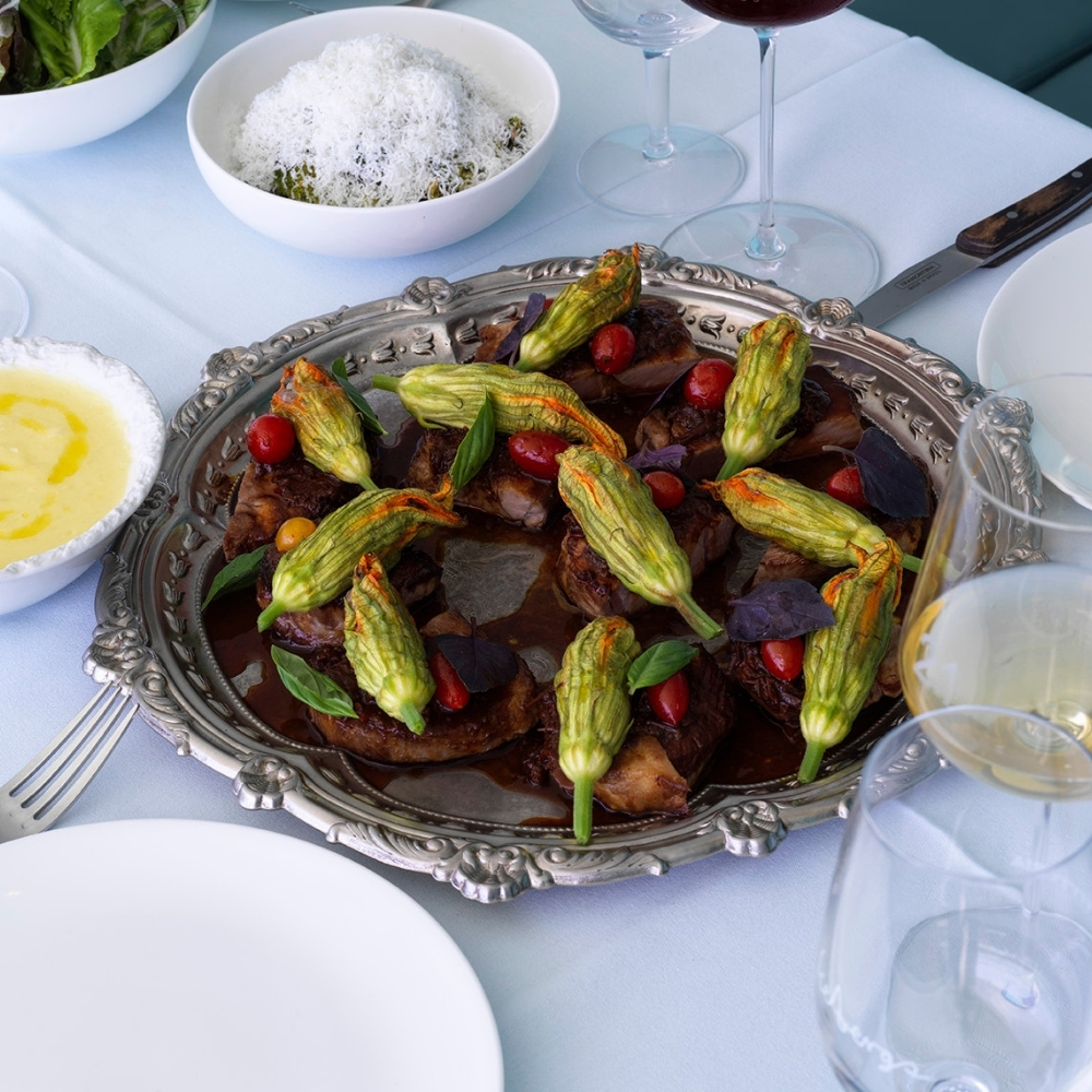 Silver platter of glazed meat with zucchini flowers on a set table